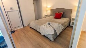 A bedroom with a bed, a nightstand, a lamp, and a door.