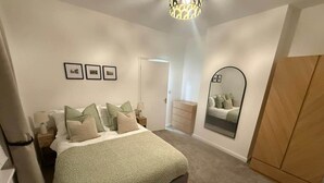 Un dormitorio con cama, mesitas de noche, cómoda, espejo y puerta.