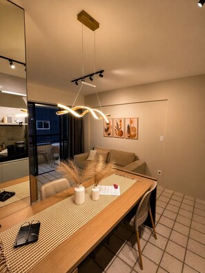 A modern living room with a dining area, a kitchen in the background, and a large mirror reflecting the space. - Apê Av. Boa Viagem Praia & restaurantes (Recife)
