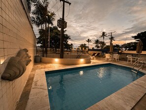 A swimming pool with a tiled deck, lounge chairs, and palm trees in the background. - Apê Av. Boa Viagem Praia & restaurantes (Recife)