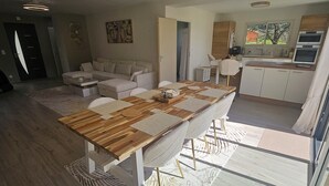 Amplia sala de estar con un gran comedor de madera, un conjunto de sofás y una cocina equipada con electrodomésticos modernos.