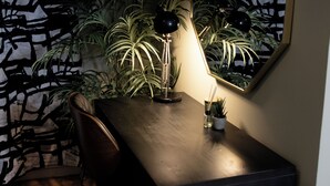 Ein dunkler Holztisch mit einer schwarzen Schreibtischlampe, einem Stuhl und einem kleinen Topfpflanzen.