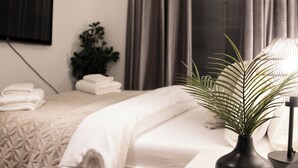 Ein ordentlich bezogenes Bett mit weißen Laken, ein Blumentopf und eine Nachttischlampe in einem Hotelzimmer.