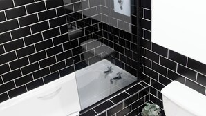 Ein modernes Badezimmer mit schwarzen Fliesenwänden, einem in Glas eingefassten Waschbecken und einer Toilette.