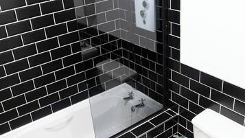 A modern bathroom with black tiled walls, a glass-enclosed sink, and a toilet.