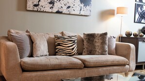 Ein beiges Sofa mit mehreren Kissen, einem Glastisch und einer Stehlampe.