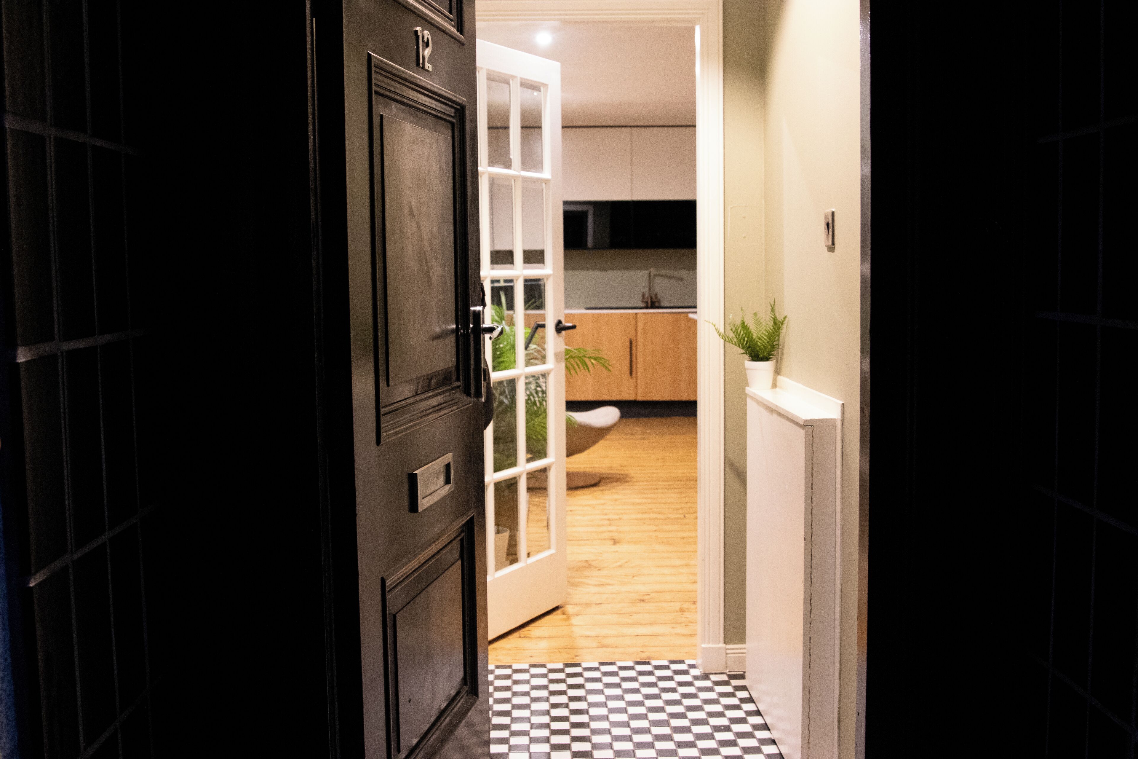 A hallway leading to a kitchen with wooden cabinets, a white door, and a checkered floor.