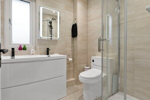 Ein modernes Badezimmer mit Duschkabine aus Glas, einer weißen Toilette und einem Waschtisch mit Spiegel.