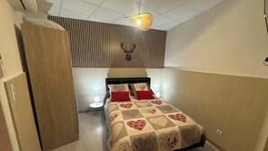 Une chambre à coucher comprenant un lit, une table de chevet, une lampe fixée au mur et une armoire en bois.
