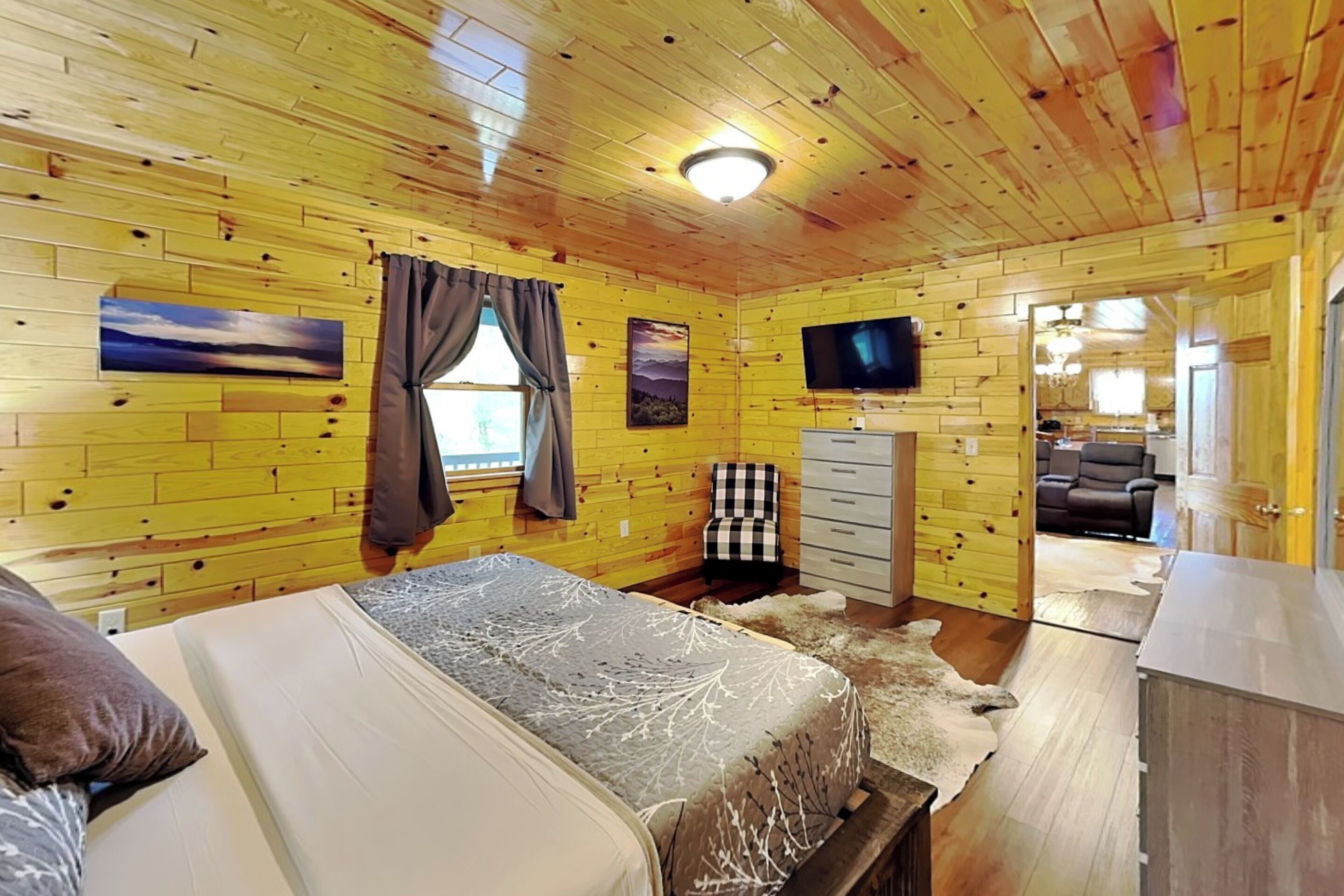 Une chambre de style cabane comprenant un lit, une commode, un téléviseur et une fenêtre avec des rideaux.