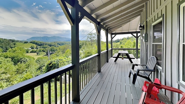 A covered porch with a view of a green landscape, a picnic table, and two chairs. - Bluff Mountain Vista (Sevierville)
