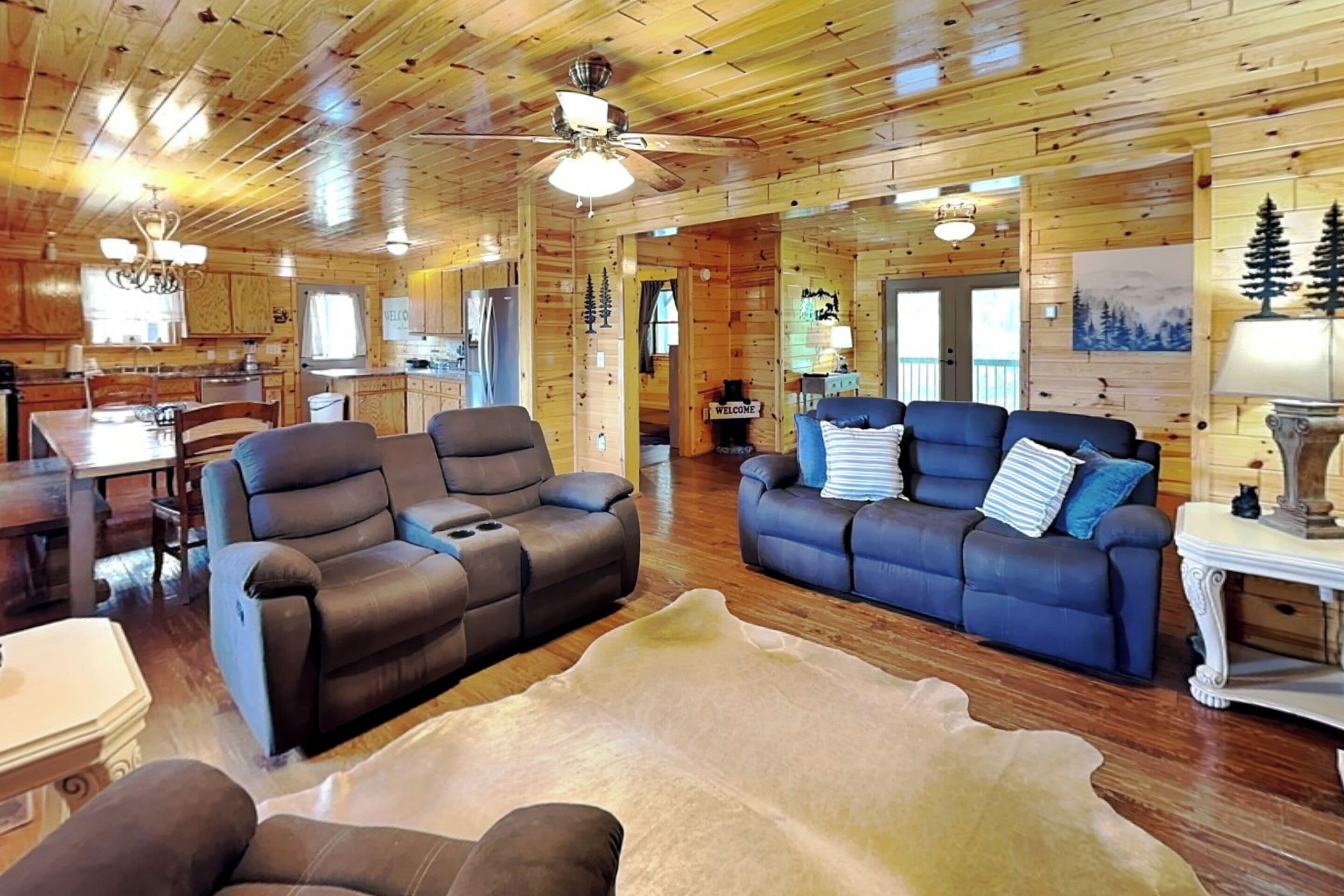 A log cabin interior with two sofas, a dining table, and a kitchen area.
