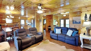 A log cabin interior with two sofas, a dining table, and a kitchen area. - Bluff Mountain Vista (Sevierville)