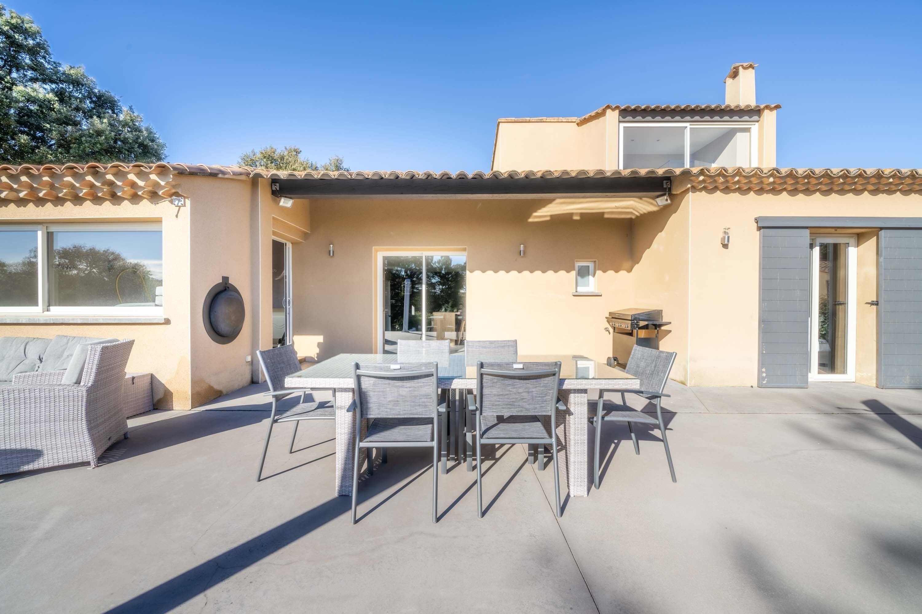 Une terrasse avec une table et des chaises pour les repas, un barbecue et un espace salon abrité.