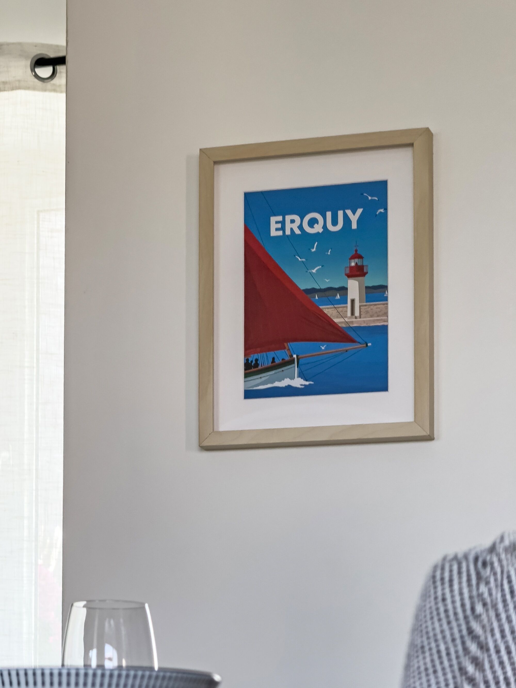 A framed picture of a sailboat with a lighthouse on a wall.