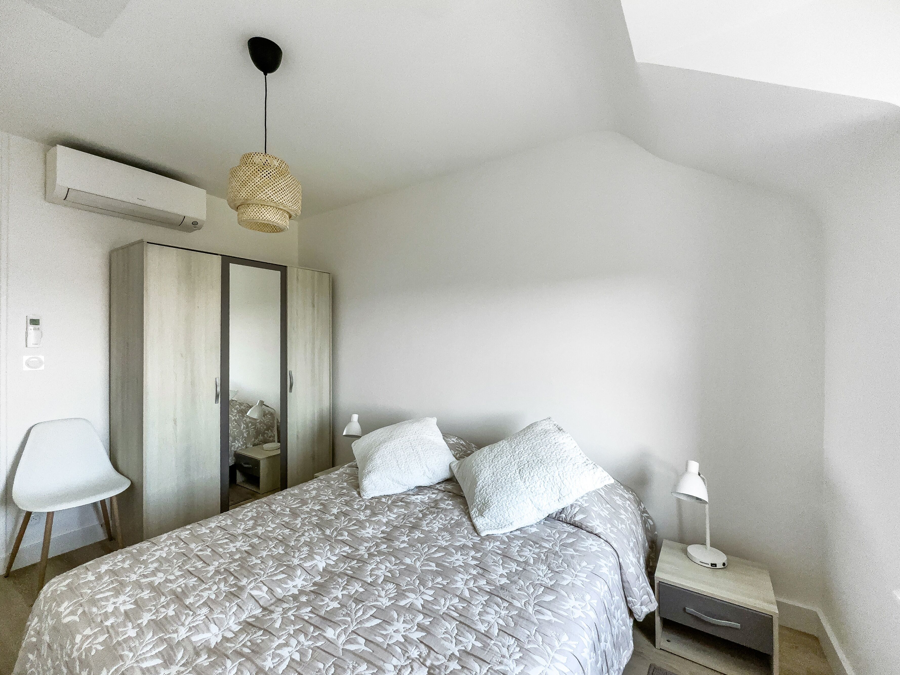 Une chambre à coucher comprenant un lit, des lampes de chevet, une armoire et un appareil de climatisation.