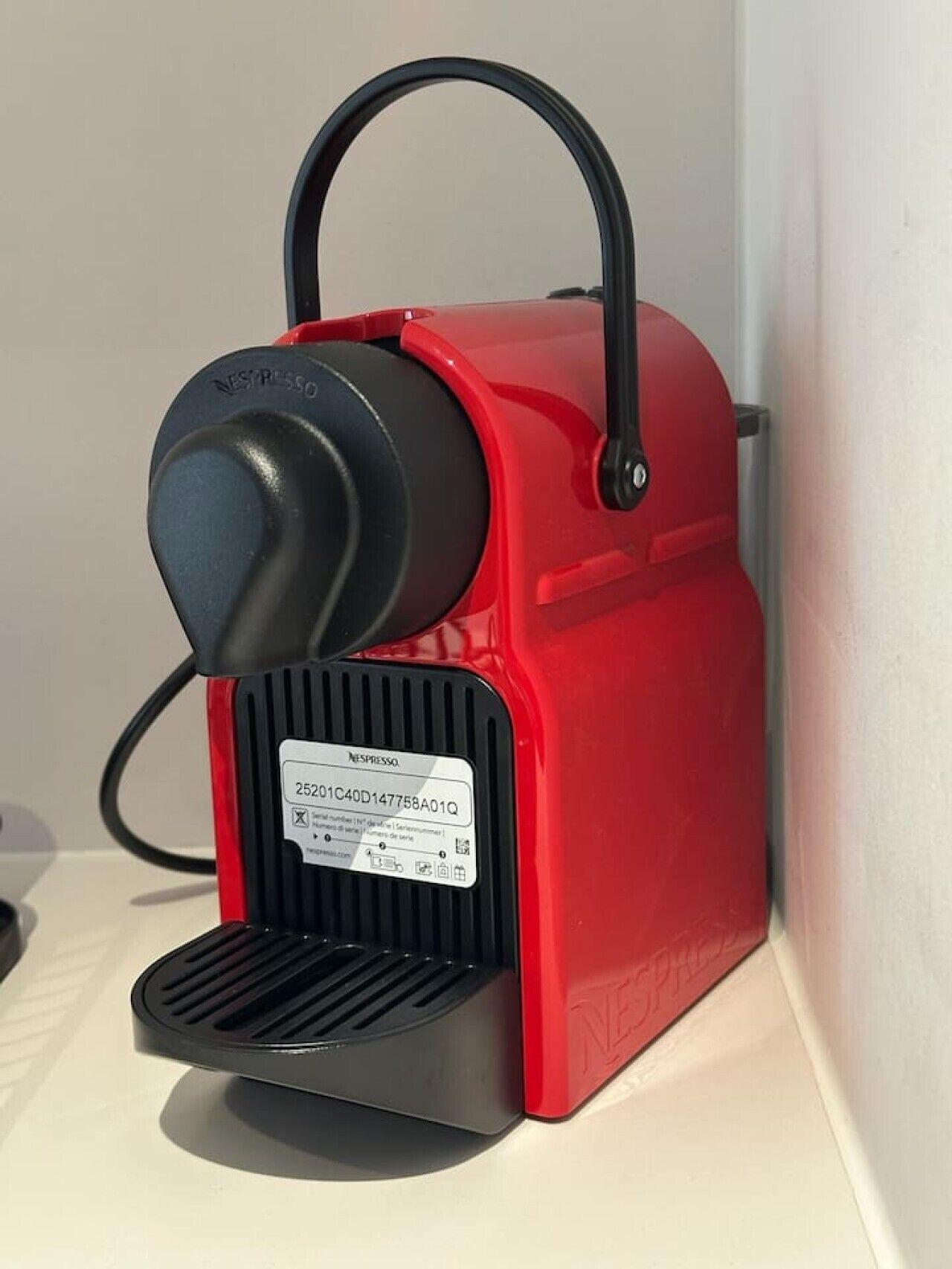 En rød og sort Nespresso kaffemaskine med etiket og ledning.