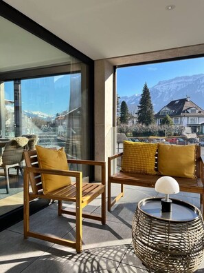 Ein Balkon mit zwei Holzstühlen und einem runden Tisch, mit Blick auf eine Berglandschaft.