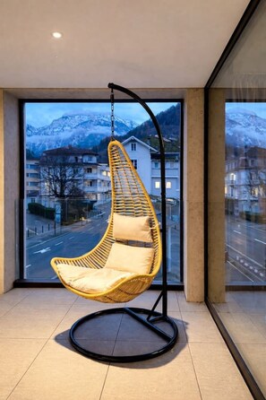 Ein Hängekorbstuhl in einem Zimmer mit großen Fenstern mit Blick auf eine verschneite Berglandschaft.