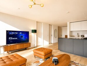 Ein modernes Wohnzimmer mit Fernseher, einer Couch, einem Couchtisch und einer Küchenzeile mit Schränken und einer Arbeitsfläche.