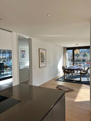 Eine moderne Küche mit dunkler Arbeitsplatte, ein Essbereich mit Tisch und Stühlen sowie ein Blick ins Freie durch große Fenster.