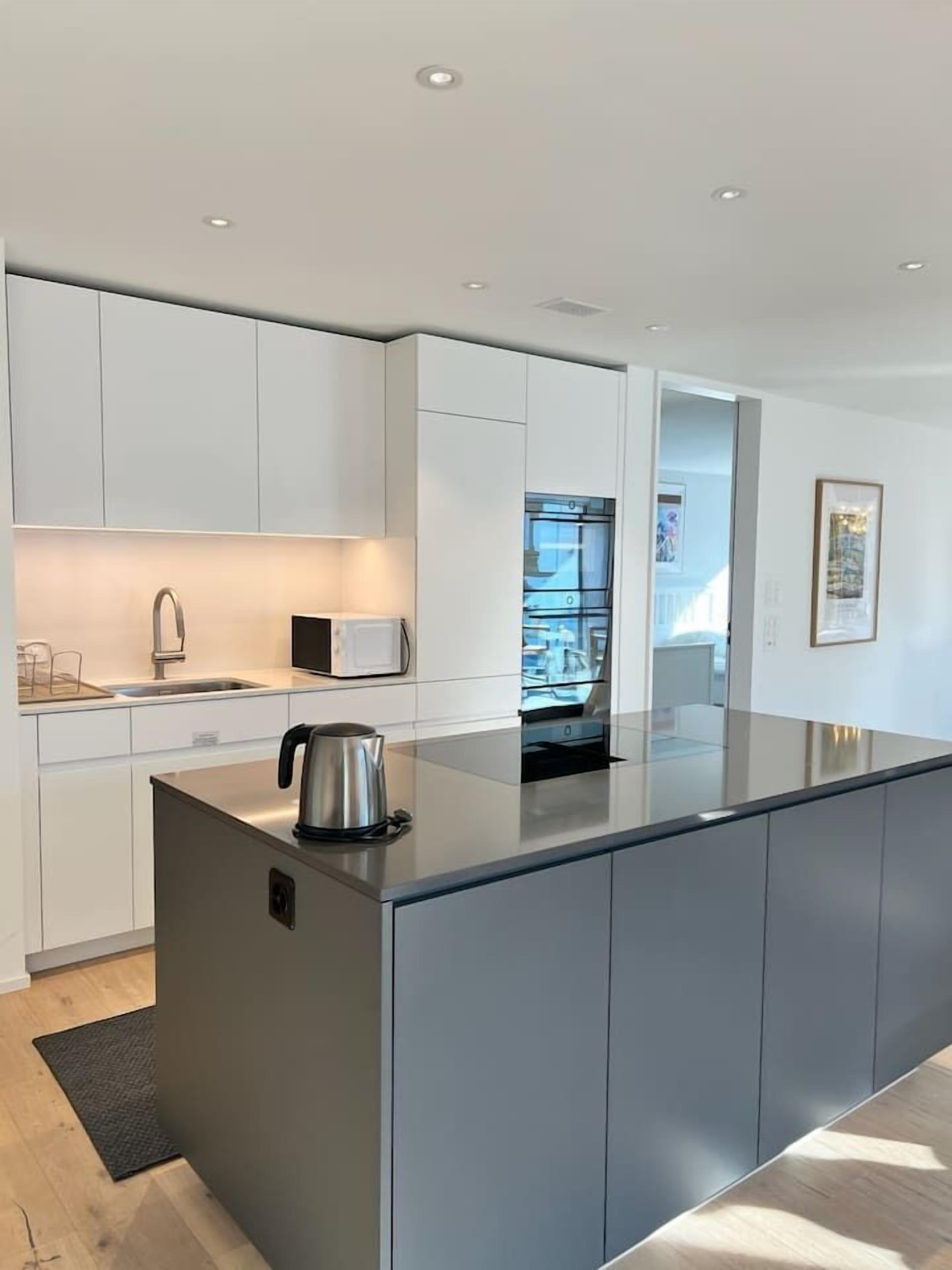 Een moderne keuken met witte kasten, een RVS-waterkoker en een inbouwoven.