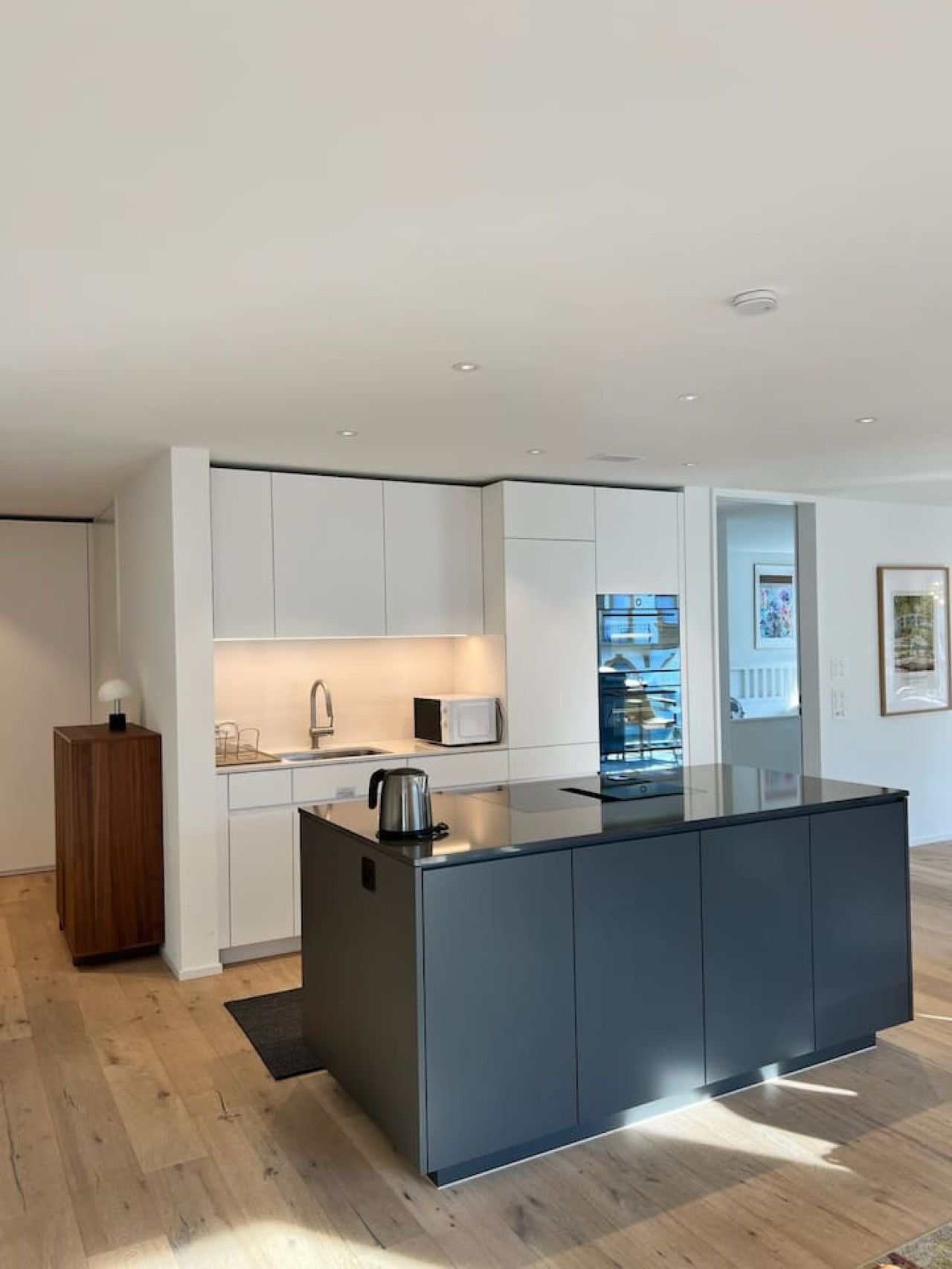 A modern kitchen with a central island, white cabinetry, and a wooden sideboard.