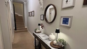 Un passadís amb una taula de consol de marbre, un mirall, diplomes emmarcades i una escala que mena a una altra habitació.