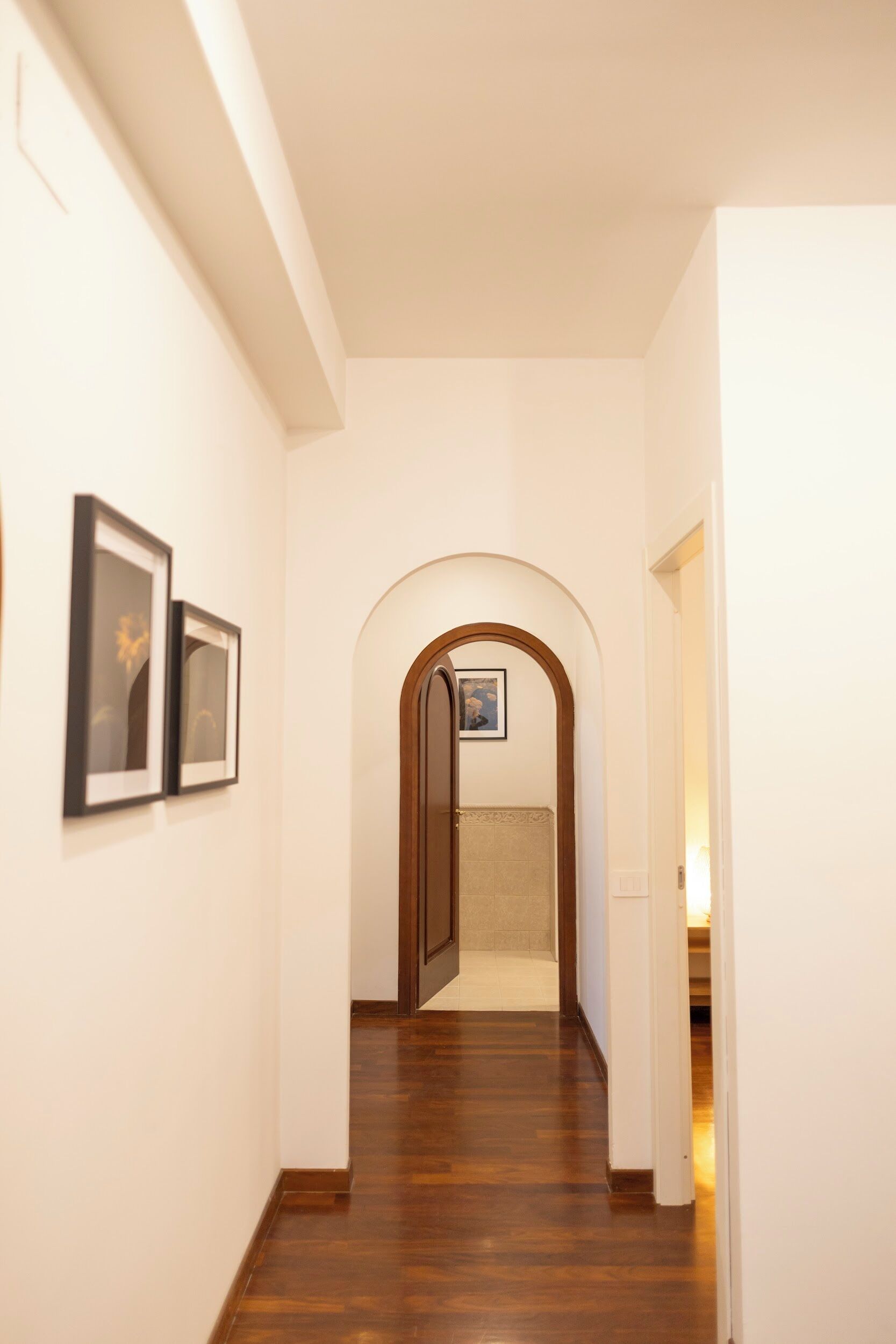 A hallway with wooden flooring, white walls, and framed artwork.