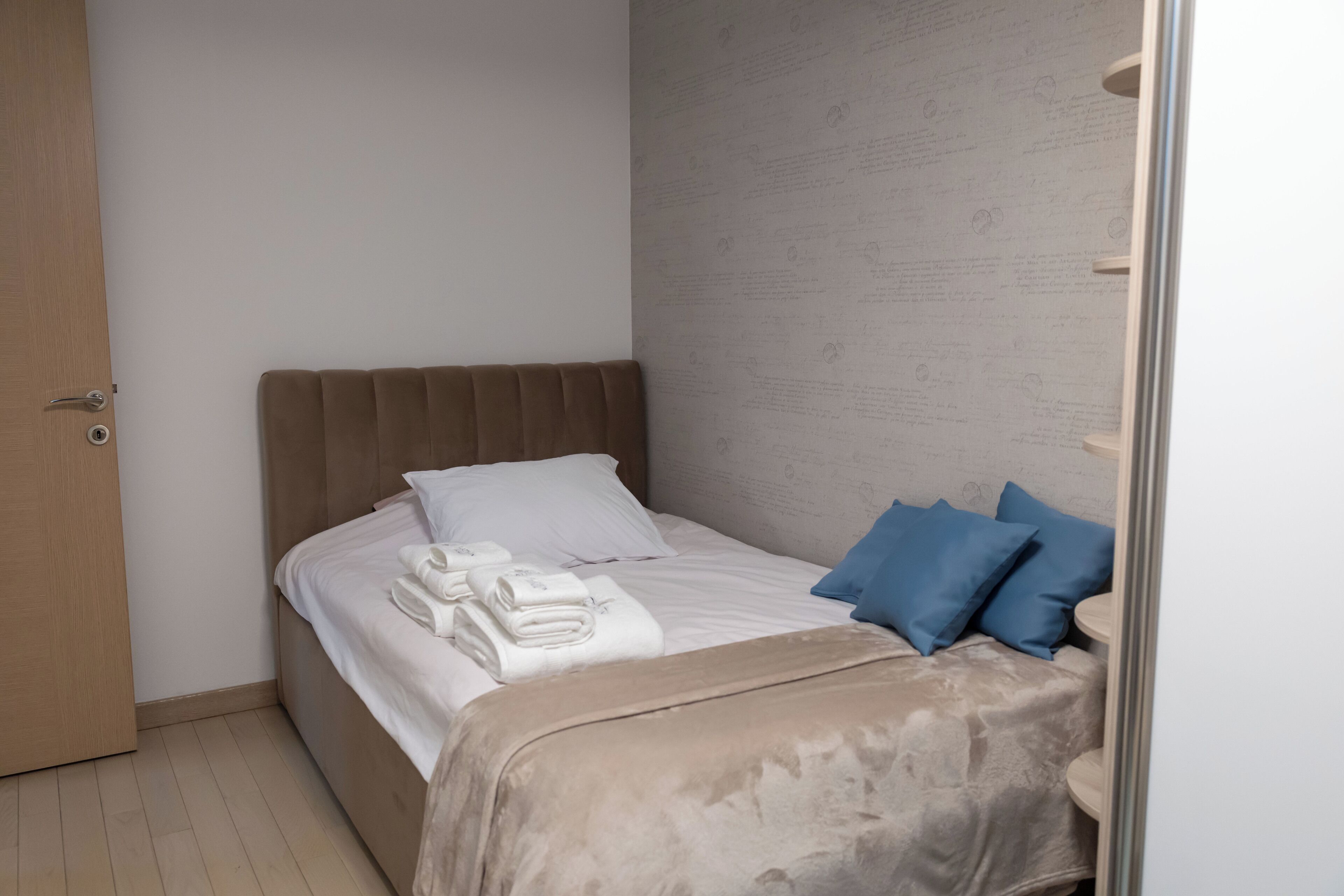 Een net opgemaakt bed met een beige hoofdbord, witte lakens en blauwe kussens.