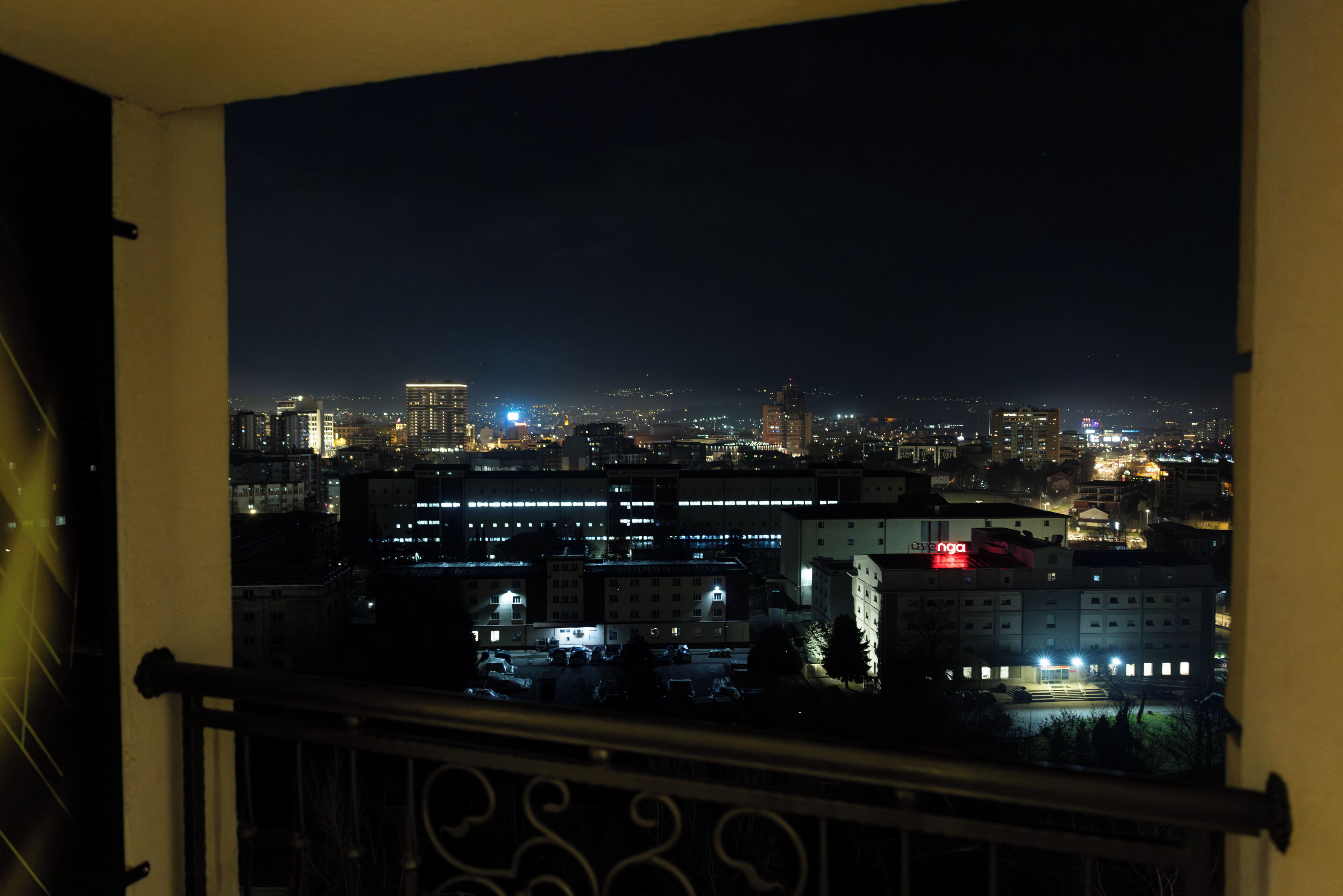 A nighttime cityscape viewed from a balcony with a railing.