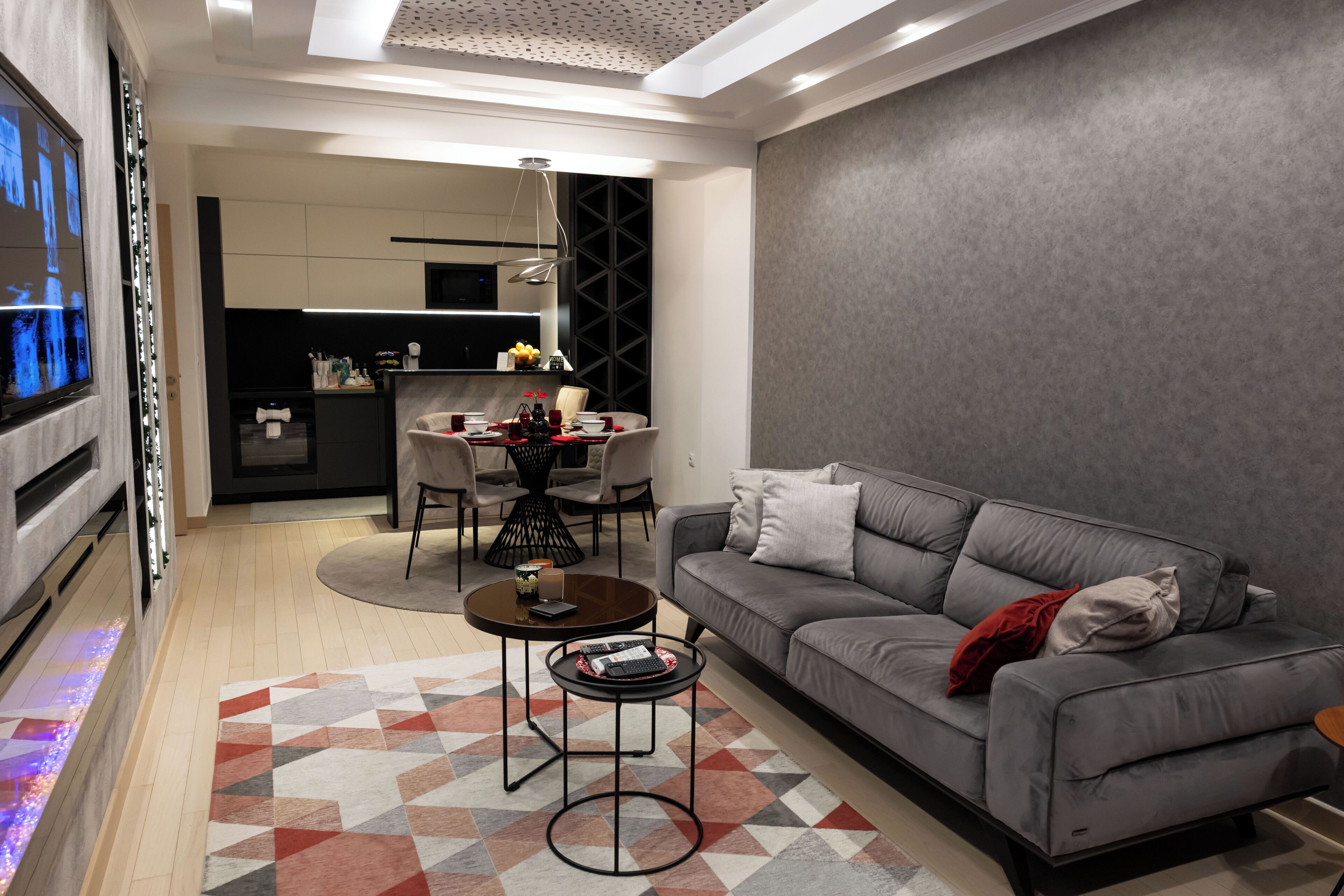 Een moderne woonkamer met een grijze bank, een salontafel en een eethoek met een kroonluchter.