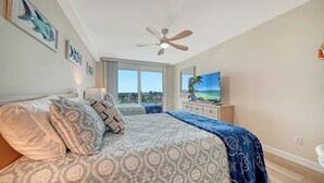 A bedroom with a bed, a ceiling fan, a TV, and a large window with a view of the ocean. - 🏝️☀️🎏 Pool, Pickle, Tennis, Beach Access all at Sun-Drenched Siesta Key Getaway⛱️🌞🐬 (Siesta Key)