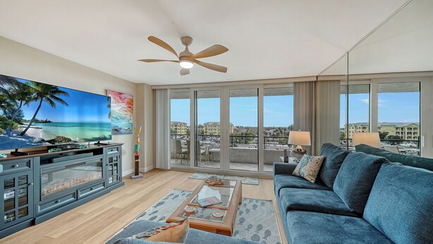 A spacious living room with a large TV, a ceiling fan, a sofa, and a balcony with a view of the city. - 🏝️☀️🎏 Pool, Pickle, Tennis, Beach Access all at Sun-Drenched Siesta Key Getaway⛱️🌞🐬 (Siesta Key)