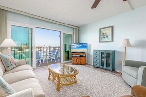Ein geräumiges Wohnzimmer mit Balkon, einem Fernseher, einem Sofa, einem Couchtisch und einem Schrank.