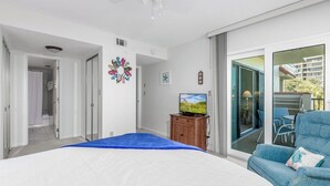 Ein Schlafzimmer mit Bett, Fernseher, blauem Sessel und einer Glastür zum Balkon.