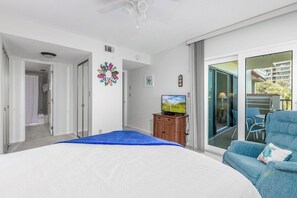 Ein Schlafzimmer mit Bett, Fernseher, blauem Sessel und einer Glastür zum Balkon.