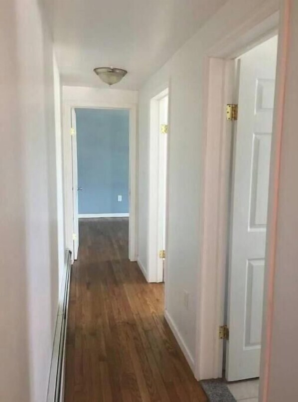 A narrow hallway with wooden flooring and white walls.