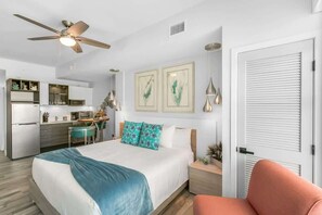 A modern hotel room with a bed, a desk, a kitchenette, and a ceiling fan. - Queen Bed Studio at Waterfront Resort (Merritt Island)