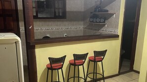 Eine Küche mit gefliestem Spritzschutz, einem Kühlschrank und drei Barhocker.
