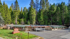 A motel with a stone facade, covered parking, and a green lawn. - Comfortable Lodge Room 12 with Extra Amenities (2 doubles, no pets) (Arnold)