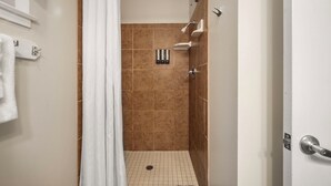 A shower area with a white curtain, a handheld showerhead, and a wall-mounted towel dispenser. - Comfortable Lodge Room 12 with Extra Amenities (2 doubles, no pets) (Arnold)