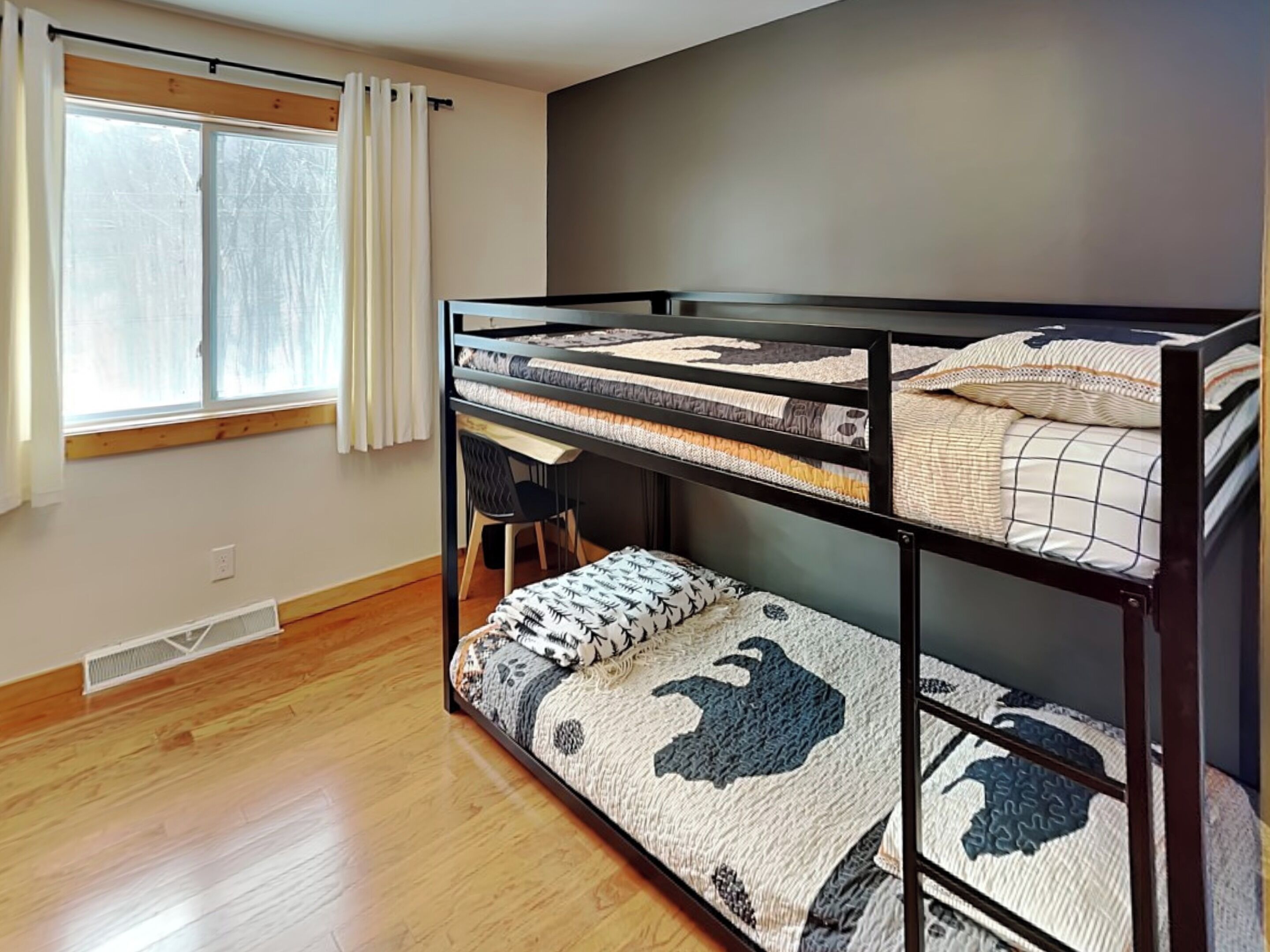 A bunk bed room with a window, a desk, and a chair.