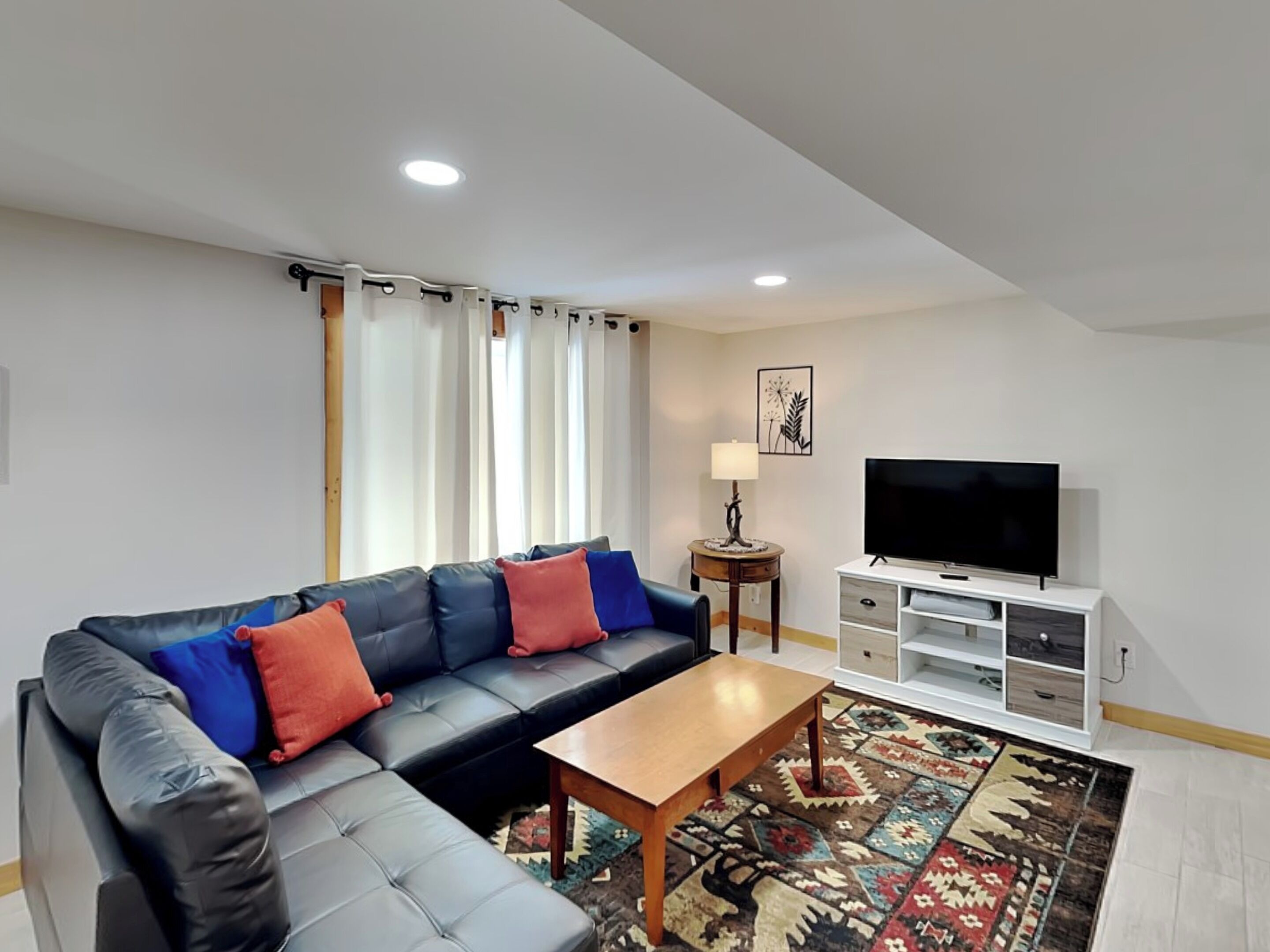 A modern living room with a sectional sofa, a wooden coffee table, a flat-screen TV, and a patterned rug.