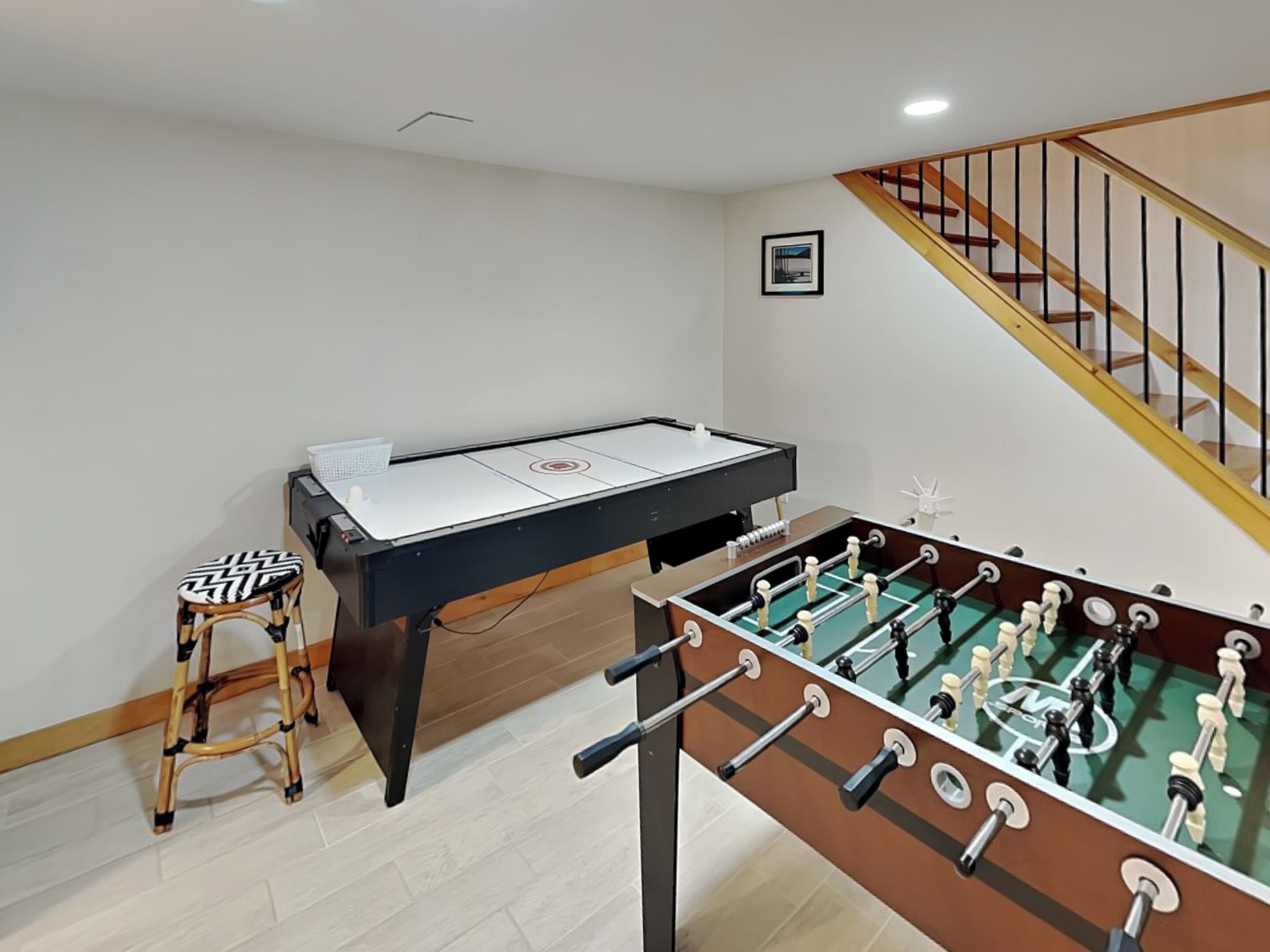 A room with a foosball table, a pool table, and a bar stool.