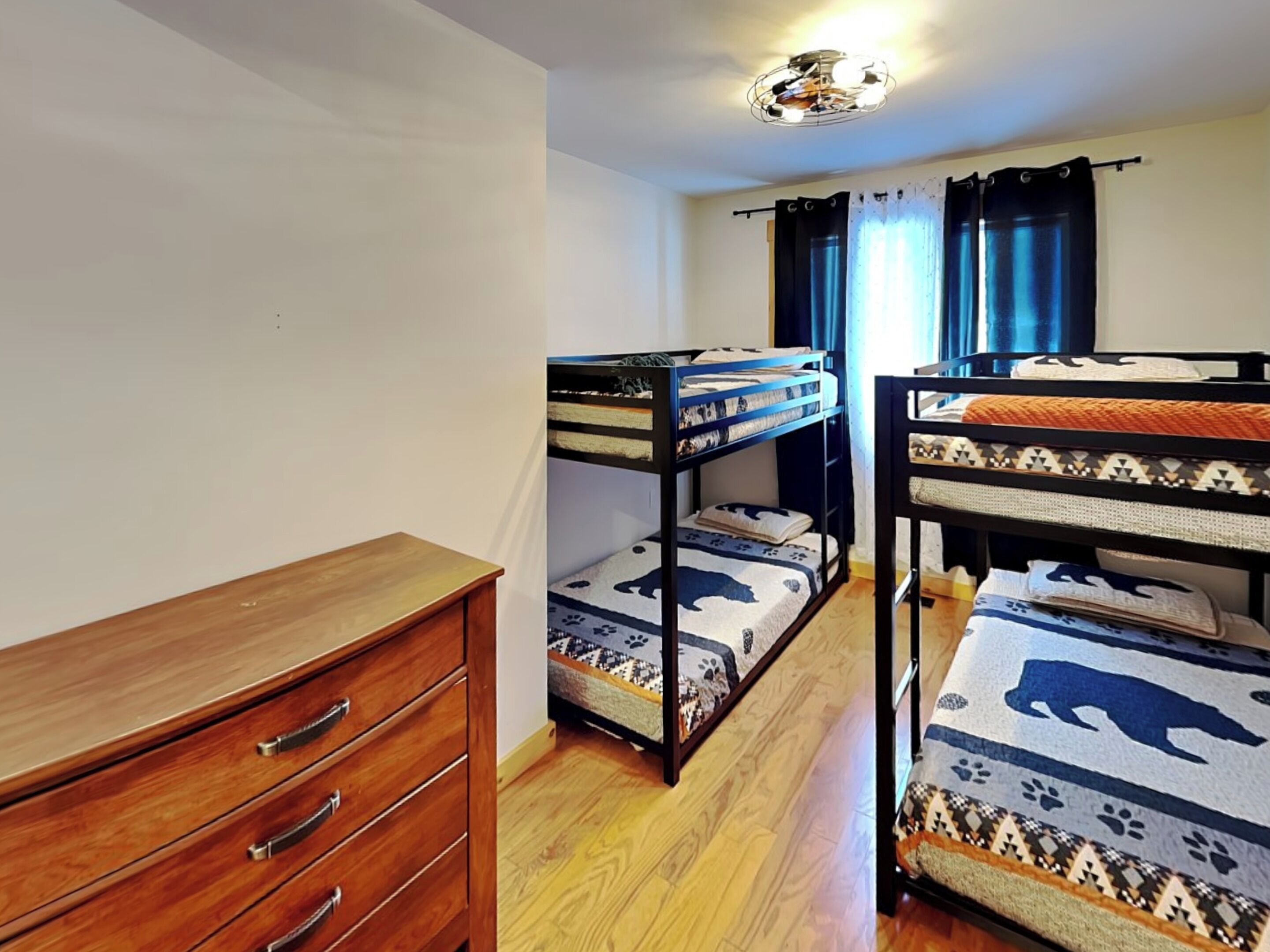 A dormitory room with bunk beds, a wooden dresser, and a ceiling light fixture.