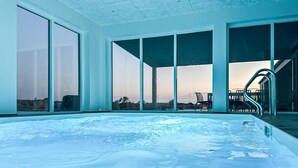 Una amplia piscina interior con paredes de vidrio transparente, vistas al paisaje y una escalera que conduce a un área exterior.