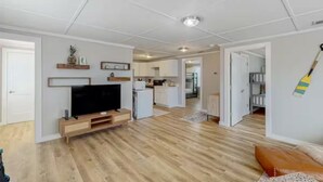 Ein modernes Wohnzimmer mit Flachbildfernseher, Holzboden und einer Küche im Hintergrund.