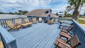 Eine Holzterrasse mit Korbstühlen und einem Tisch, mit Blick auf eine Wohngegend mit Häusern und einer Palme.