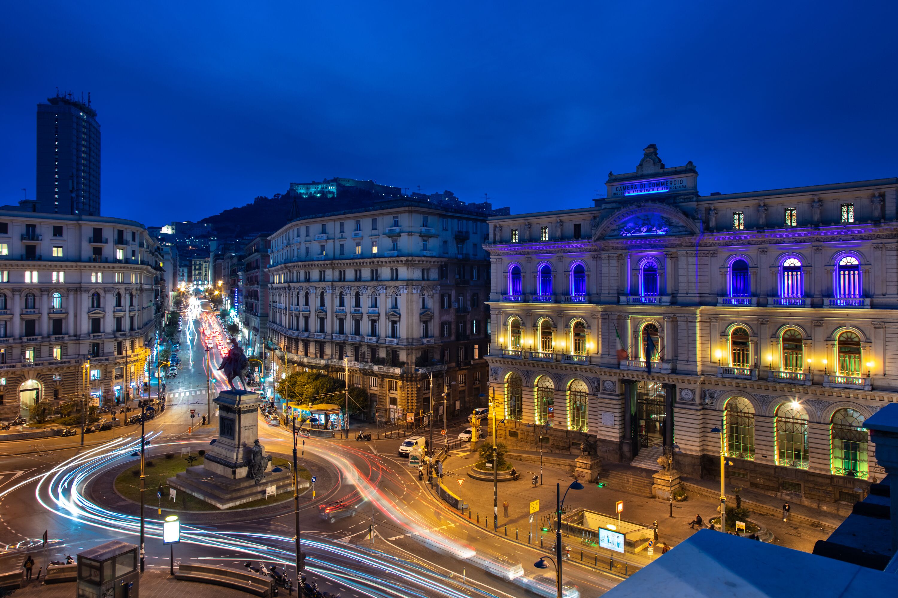 Um edifício histórico com arquitetura clássica, uma rotatória central e postes de iluminação modernos.